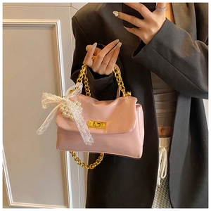 Close-up of pink leather handbag featuring gold chain handle and pearl lace bow detail