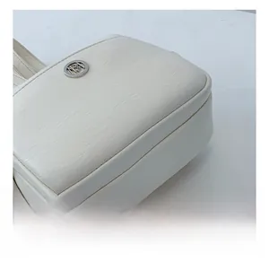 Dettaglio della texture in pelle bianca martellata con logo circolare in metallo