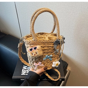 Détail d'un sac en paille tressée avec ours en peluche, nœuds et cordon de serrage