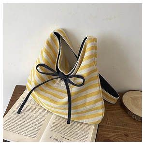Detail of yellow and white striped canvas tote bag with black bow and woven brand label