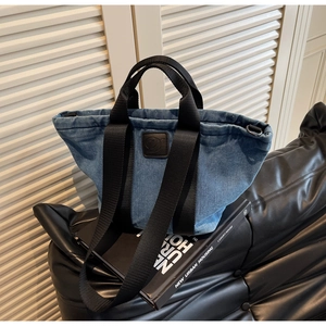 Détail du sac fourre-tout en denim bleu avec logo en cuir noir et anses en nylon