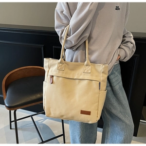 Close-up of beige canvas tote bag with brown leather brand tag and blue fabric detail