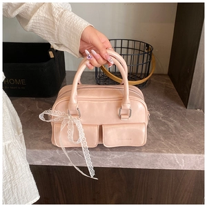 Detail of pink faux leather handbag featuring twin front flap pockets and white lace bow
