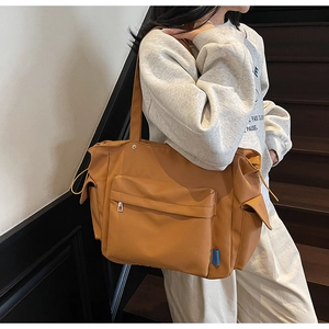 Detail view of a large brown canvas tote bag with front zipper and side pockets