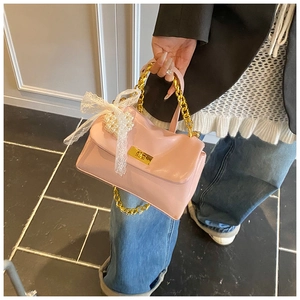 Detail of pink handbag featuring gold chain, pearl charms, and white lace bow decoration