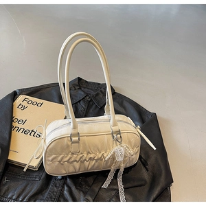 Detail of a creamy white pleated shoulder bag with lace and pearl charms on a black jacket