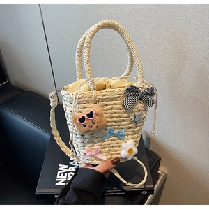 Détail du sac seau en paille tressée à la main avec breloques florales et décor d'ours
