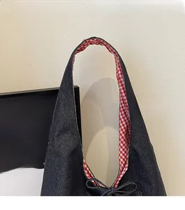 Detail of blue denim tote bag with red gingham lining and decorative bow on the strap
