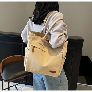 Detailed view of beige canvas tote bag with leather logo patch and shoulder straps