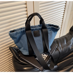 Détail du sac cabas en denim bleu avec bandoulières en nylon noir et logo sur meuble en cuir