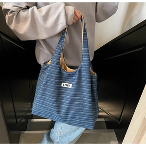 Detail van blauw gestreepte canvas draagtas met LOVE-patch gedragen in zijwaartse stijl