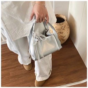 Detail of silver tote bag with textured leather and a white lace bow on handle