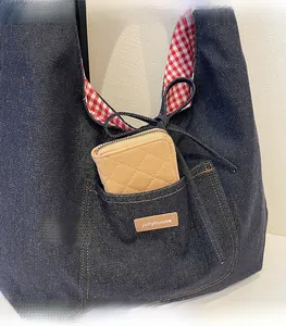 Detail of denim tote bag featuring a front pocket with a leather tag and red checkered lining