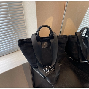 Détail du sac cabas en toile noire avec écusson en cuir, poignées et large bandoulière