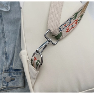Detail of detachable floral embroidered strap and silver metal hardware on white bag