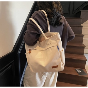 Detail shot of a cream canvas tote bag showing side pocket and leather logo patch