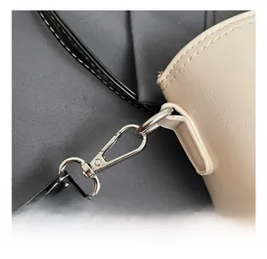 Macro detail of the silver metal swivel hook and black leather strap on a beige bag