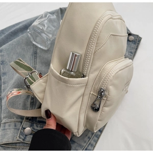 Close-up of beige nylon crossbody bag with zipper detail on denim jacket background