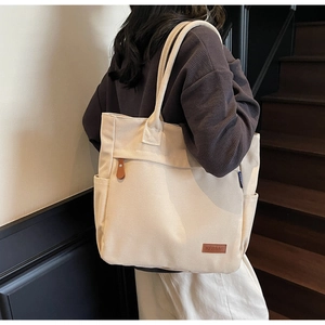 Detailed view of beige canvas tote bag featuring side pocket and brown leather logo tag