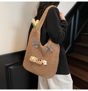 Détail du sac cabas en paille tissée avec nœuds à carreaux et breloques en peluche