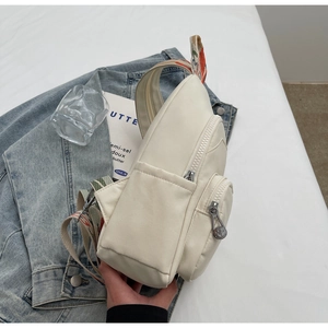 Detail showing cream multifunctional chest bag with colorful woven strap on denim jacket