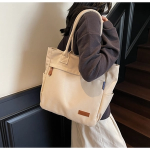 Detail of spacious cream canvas tote bag with leather tag and shoulder strap on model