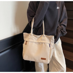 Detail of canvas tote bag showing side pocket, leather logo patch and texture