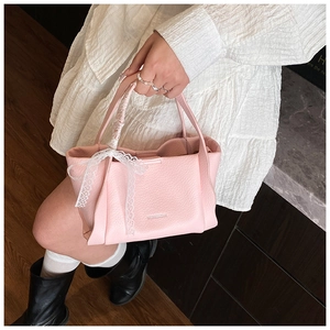 Close-up of pink lychee grain leather handbag with white lace bow and metal logo detail