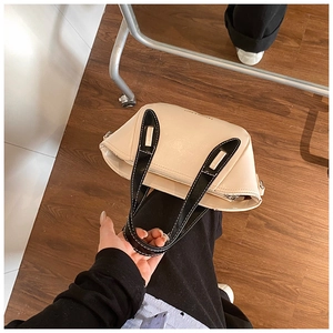 Detailed close-up of beige leather bucket bag featuring black handles with white stitching