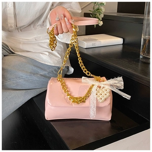Detailed view of pink shoulder bag with gold chain, lace bow and pearl heart charm