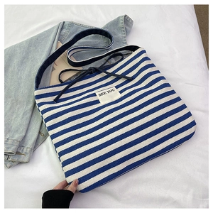 Detail of blue and white striped canvas tote bag with 'SEE YOU' patch on a casual background