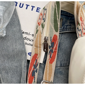 Detail of multi-color ethnic floral embroidery on a woven bag strap with silver metal zipper