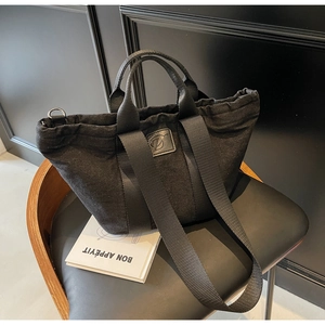 Détail du sac cabas en denim noir avec écusson en cuir D et fermeture par cordon de serrage