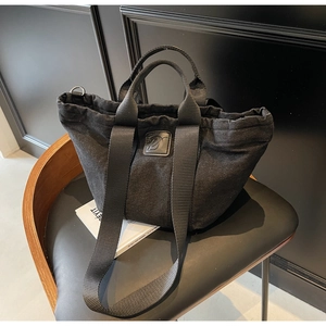 Détail du sac cabas en denim noir avec fermeture à cordon et logo D en cuir gaufré