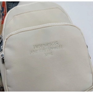 Close-up of beige fabric chest bag with 'NEW DREAMS' embroidery and metal zipper