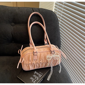 Detail of pink pleated cylinder bag with pearl lace bow charm on dark corduroy sofa