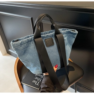 Détail du sac cabas en denim bleu clair avec patch logo noir et larges bandoulières