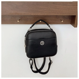 Dettaglio borsa in pelle nera opaca con logo argento circolare appesa a gancio di legno