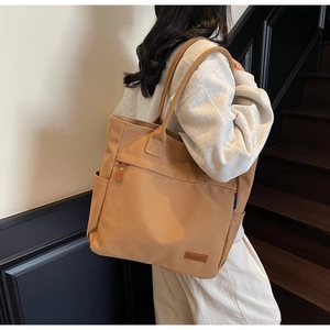 Detail of khaki canvas tote bag featuring a front zipper pocket and side water bottle slot
