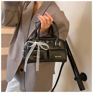 Detail of black glossy leather bag with white lace bows and polished silver hardware