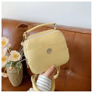 Dettaglio della mini borsa in pelle gialla con logo metallico tondo e trama della tasca
