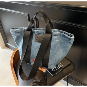 Détail du sac fourre-tout en denim bleu clair avec anses noires et logo en cuir