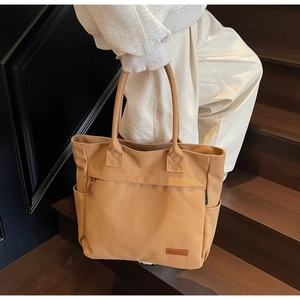 Detail of khaki canvas tote bag showing side pocket and leather logo patch on stairs