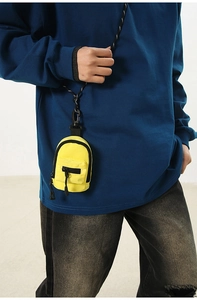 Close-up of bright yellow mini backpack pouch worn with a woven lanyard across the body