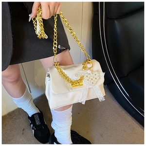 Detail of a creamy leather crossbody bag with gold chain and pearl heart lace charm