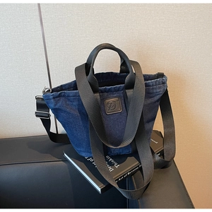 Détail du sac cabas en jean bleu avec sangles en nylon noir et écusson logo en cuir