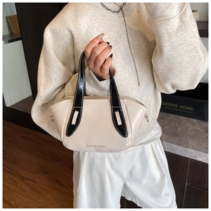 Detail view of a beige leather bucket bag with black handles and metal chain strap