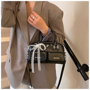 Detail of black glossy handbag with lace bows and utility pockets worn with a grey blazer