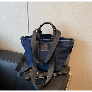 Détail macro du cabas en denim bleu foncé avec patch logo en cuir et anses noires
