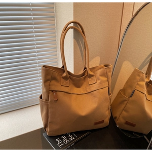 Detail of canvas tote bag showing side pockets, reinforced handle and brand label